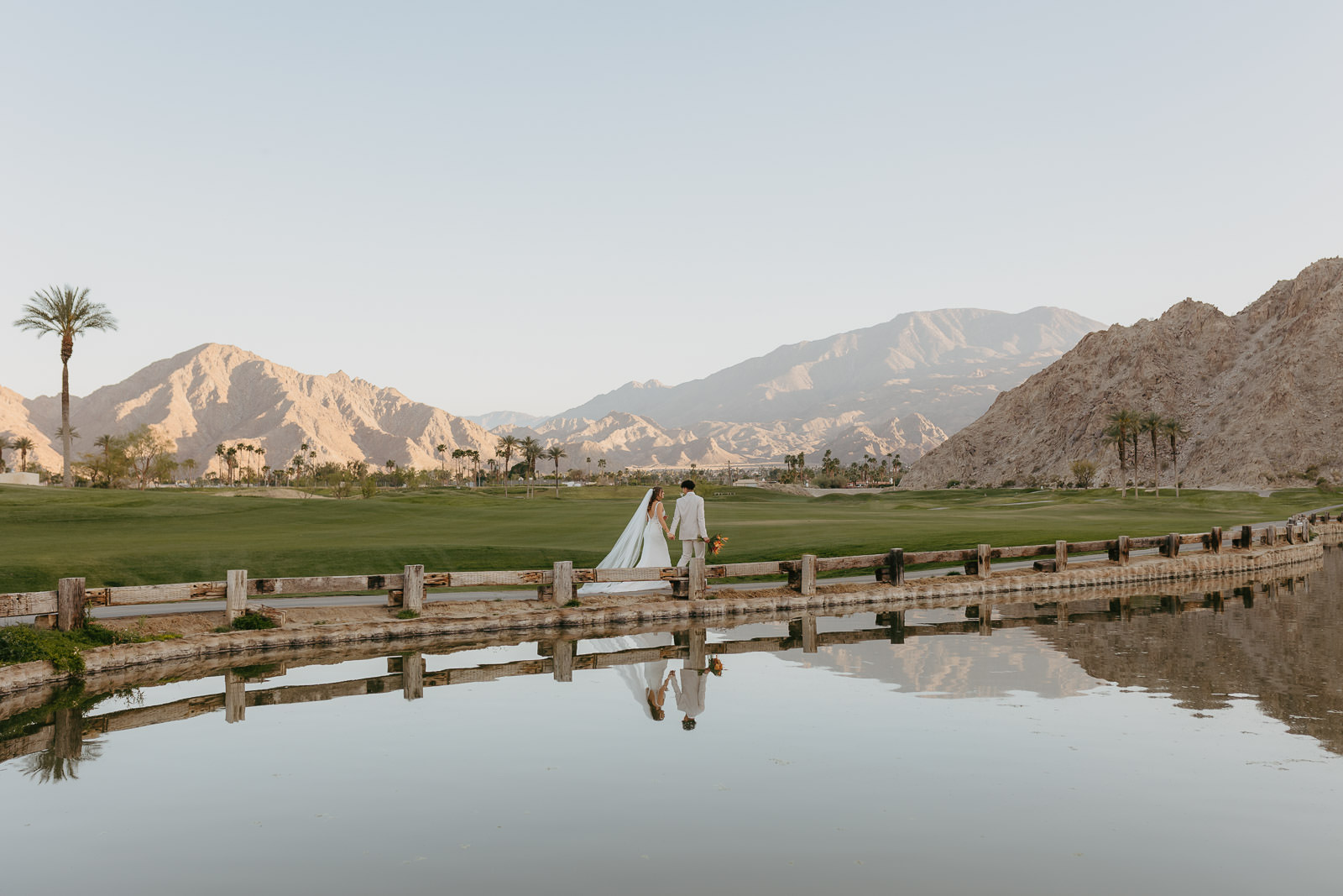 bride and groom walk along venue PGA West with desert mountains in background